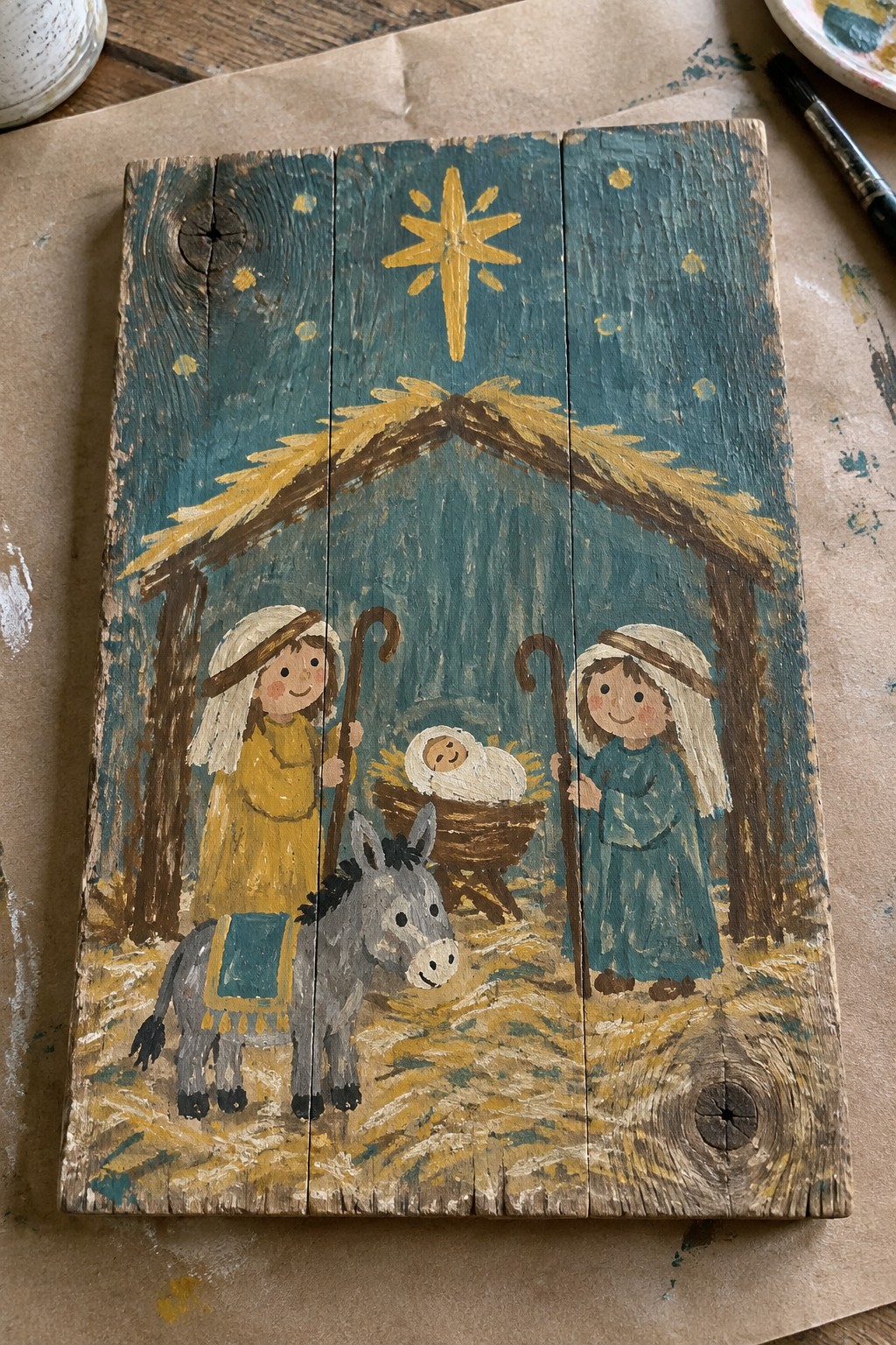 Folk-art nativity on wood showing Mary in yellow, Joseph in blue, donkey, manger, and star.