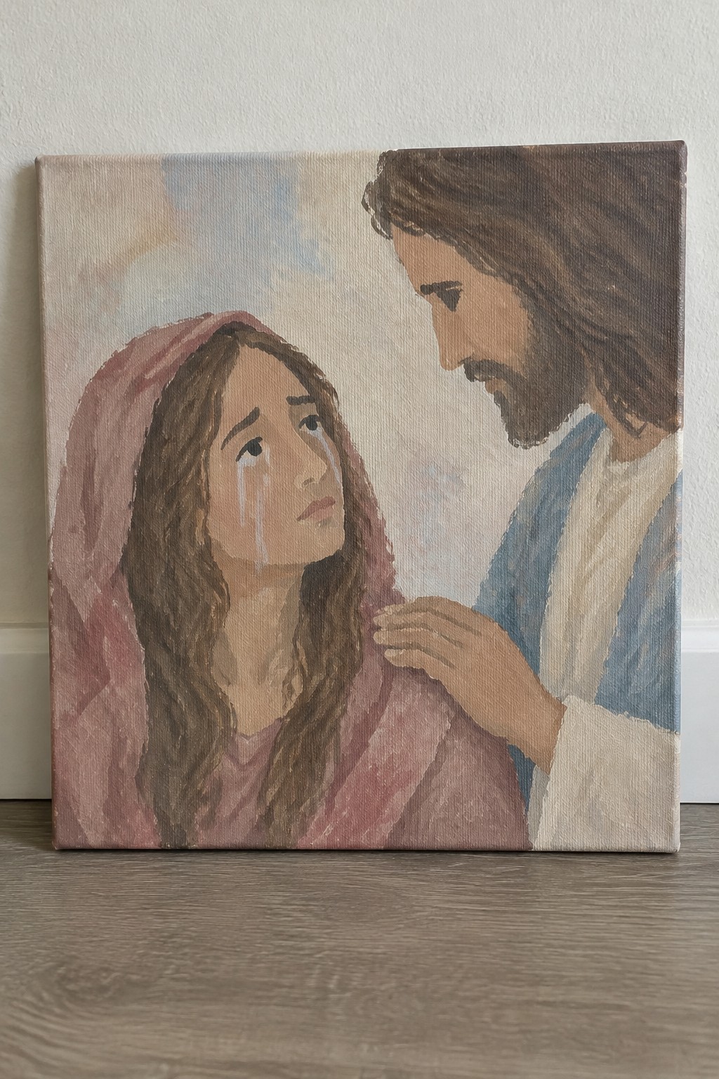 Canvas painting of crying woman in pink robes comforted by bearded man in blue.