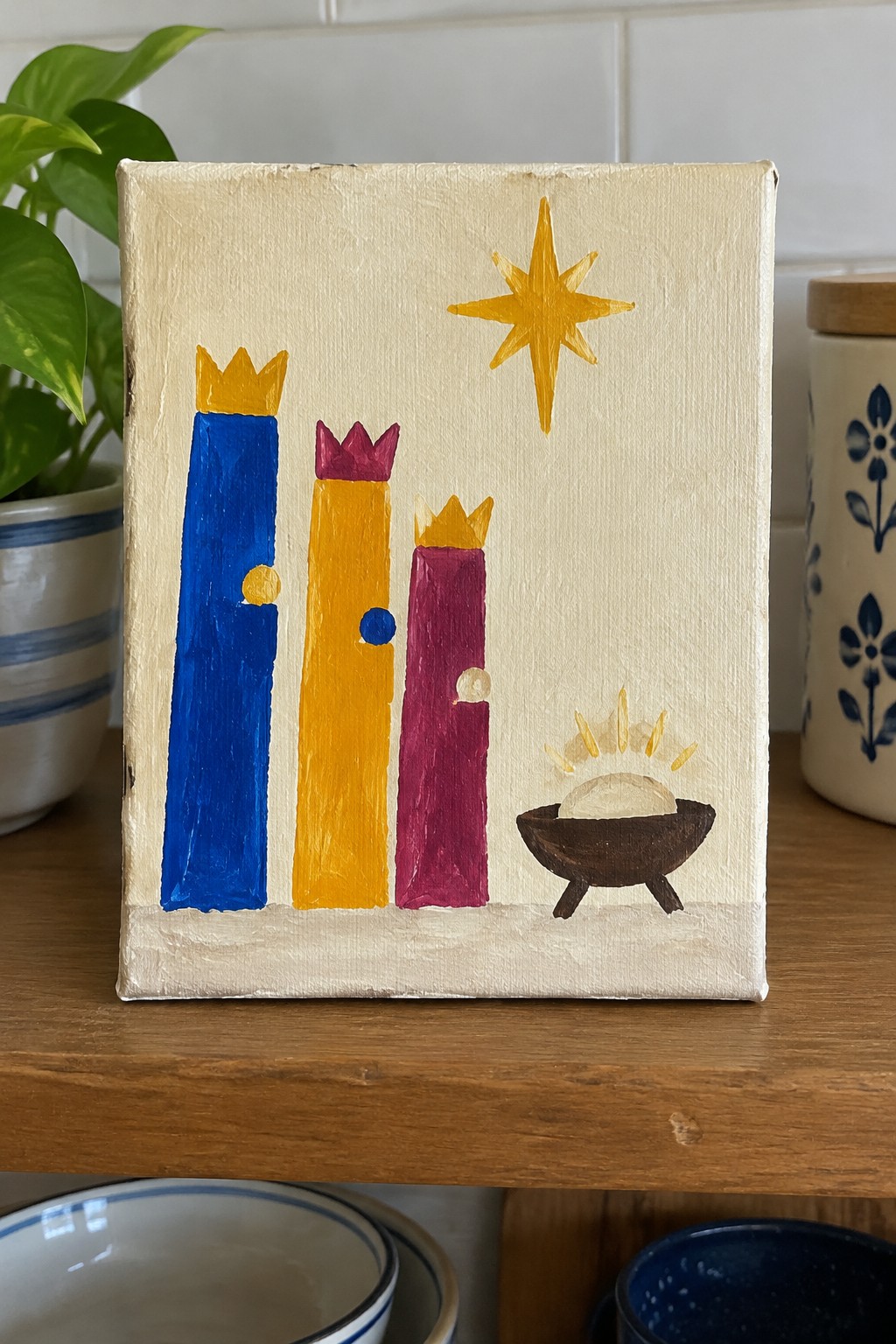 Three crowned figures in blue, yellow, and purple with star and manger painting