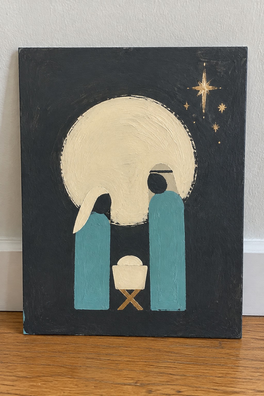 Abstract painting of two teal-robed figures with manger under large moon and gold stars