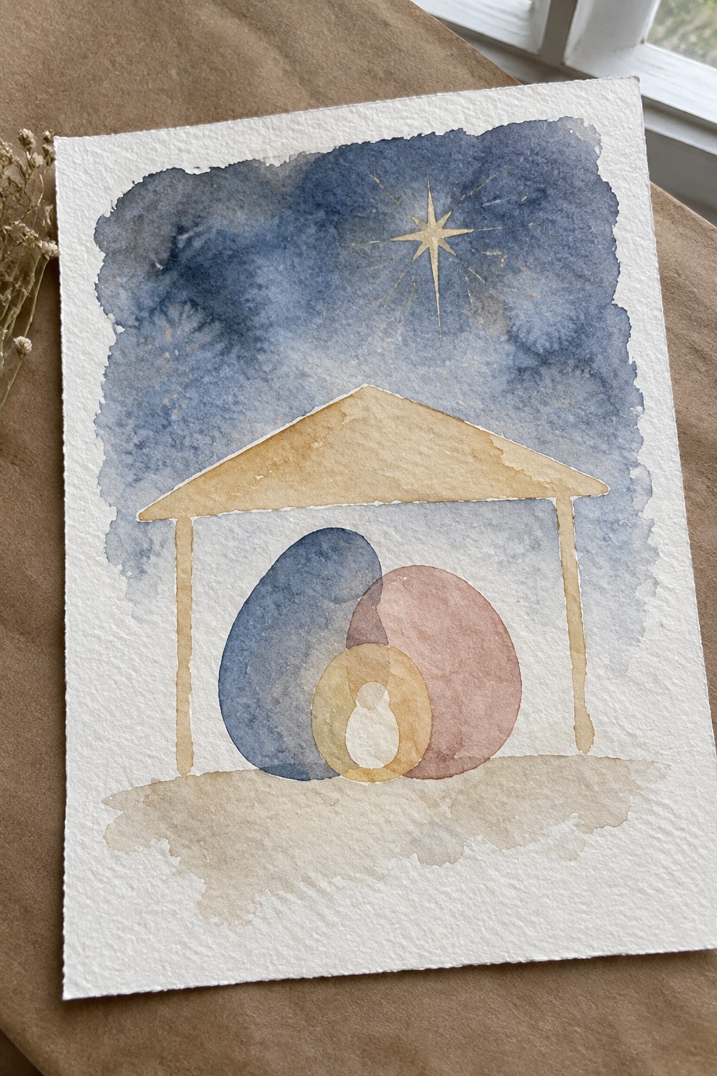 Watercolor nativity with golden star above tan stable and abstract figures