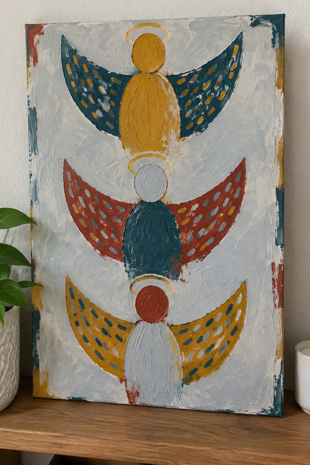 Abstract painting of three stacked angels with dotted colorful wings and golden halos.