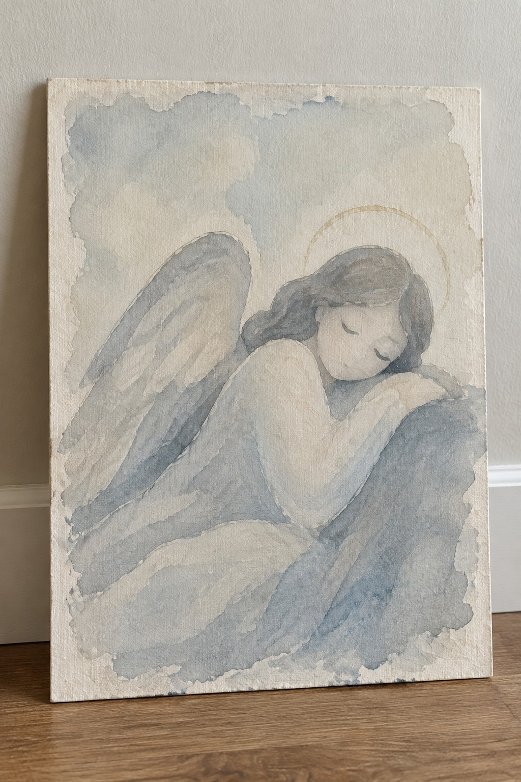 Watercolor angel with wings and halo resting on soft blue clouds.