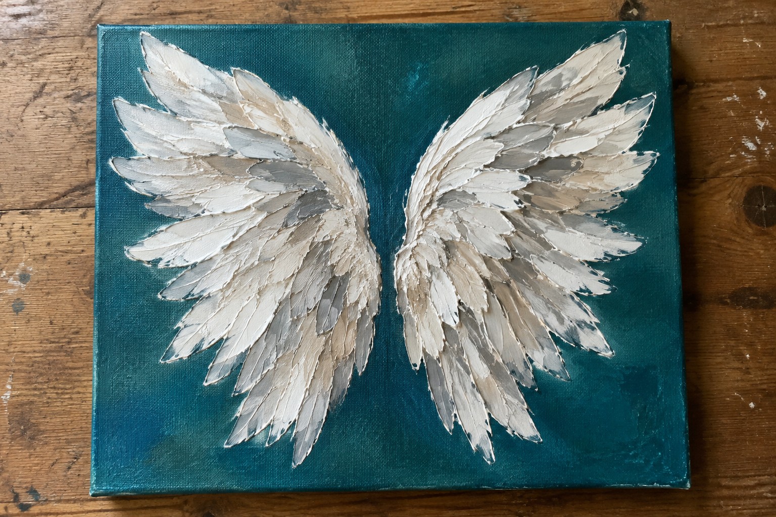 Two textured white and gray angel wings on a teal canvas over wood