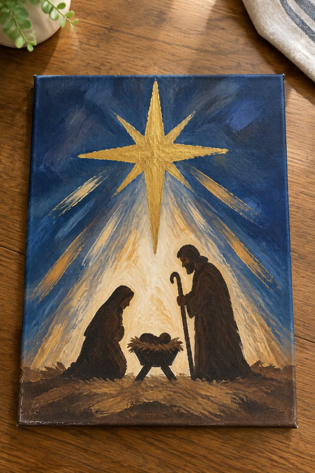 Nativity painting with Mary kneeling, Joseph by manger under golden star with light rays